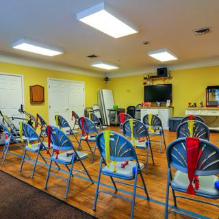 A well-lit classroom with rows of blue chairs, a television on the wall, and bright yellow walls.