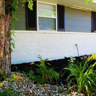 A neatly landscaped garden area with various plants and a stone border in front of a house.