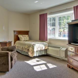 A cozy bedroom featuring a single bed, television, and large window with curtains.