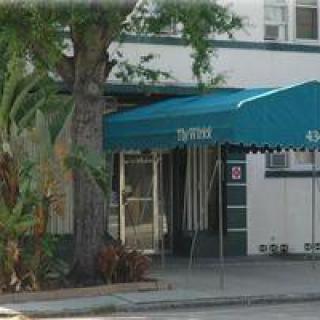 An entrance with a blue awning beside a tree on a sidewalk.