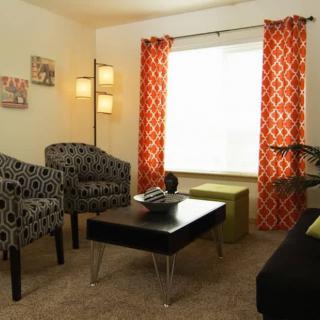 A modern living room with patterned curtains, stylish armchairs, and a sleek black coffee table.