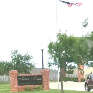 An entrance sign with a flag flying above it, surrounded by greenery.