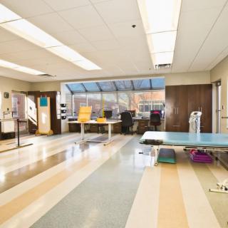 A well-lit office space with multiple desks and chairs, featuring large windows allowing natural light.