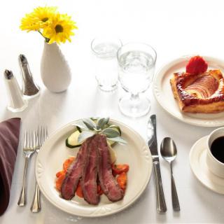 A breakfast table setting with bacon, a pastry, coffee, and yellow flowers.