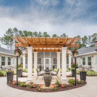 A beautiful outdoor courtyard featuring a wooden pergola, lush landscaping, and a tranquil setting.