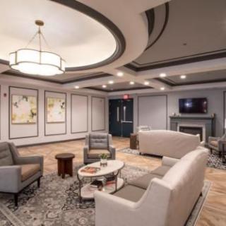 A modern lounge area with comfortable seating, artwork on the walls, and a central chandelier.