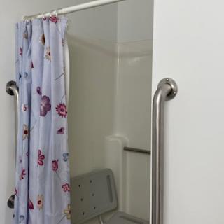 Accessible shower setup with a curtain, grab bars, and a folding chair.