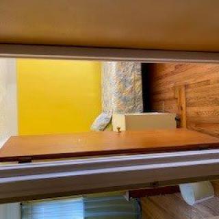 A view through an open doorway into a bedroom with a yellow wall and wooden flooring.