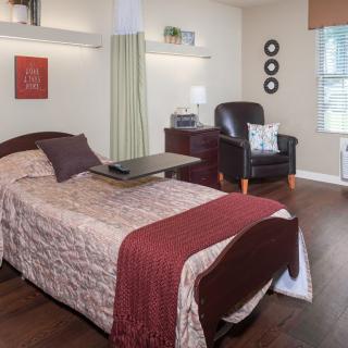 A cozy bedroom with a bed and a comfortable chair beside it, featuring warm decor and soft lighting.