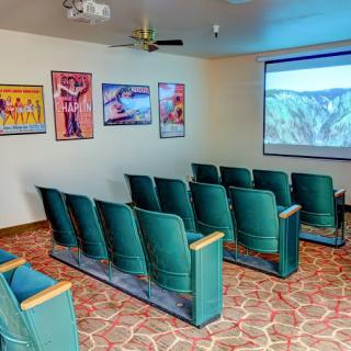 A cozy home theater setup with rows of seats, a projector screen, and movie posters on the wall.