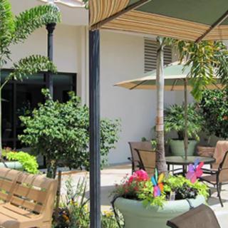 A serene garden patio with comfortable seating, lush plants, and large umbrellas providing shade.