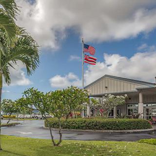 A building with an American flag flying outside, surrounded by palm trees and greenery under a cloudy sky.