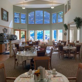 A spacious dining area with large windows letting in natural light, featuring neatly arranged tables and chairs.