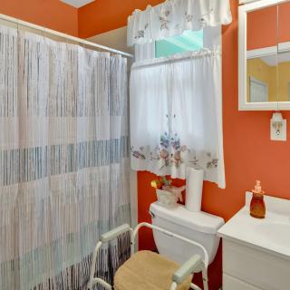 A cozy bathroom with vibrant orange walls, featuring a shower curtain and a small window with lace curtains.