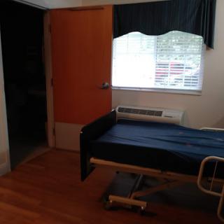 A hospital room featuring a bed, window, and wooden flooring.