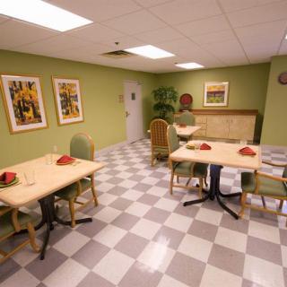 A cozy dining area featuring simple tables and chairs against a green backdrop, complemented by decorative artwork.
