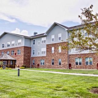 A large residential building with a well-maintained lawn and trees under a partly cloudy sky.