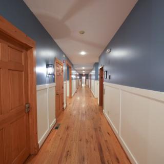 A long hallway with wooden floors and blue walls, lined with doors on either side.