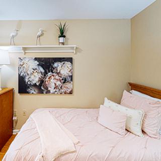 A cozy bedroom with a neatly made bed, decorative artwork, and a small plant on a shelf.
