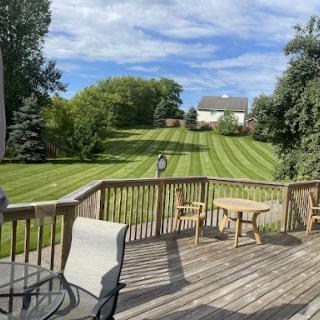 A serene view from a deck overlooking a neatly manicured lawn and trees under a blue sky.