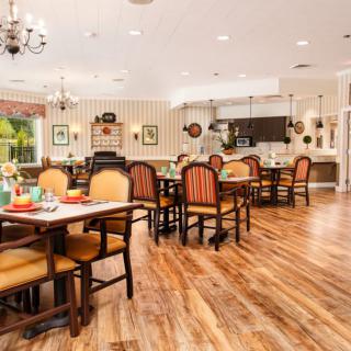 A cozy dining area with neatly arranged tables and chairs, featuring a warm wooden floor and elegant decor.