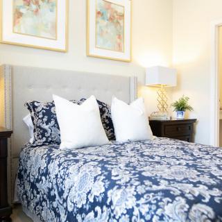 A cozy bedroom featuring a stylish bed with floral bedding and white pillows, complemented by elegant artwork and bedside lamps.