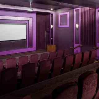 A cozy cinema room with purple lighting and rows of comfortable seating facing a large screen.