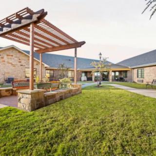 A beautifully landscaped garden featuring a wooden pergola and a well-maintained lawn in the courtyard of a brick building.