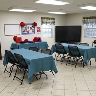 A classroom setup with tables and chairs, featuring a large television and decorative elements.