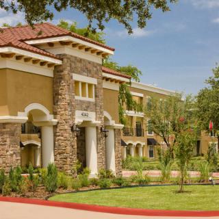 A sunny day view of a beautiful building with stone and stucco architecture surrounded by trees and grass.