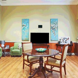 A cozy living room with a round wooden table, chairs, and a large television surrounded by colorful artwork.