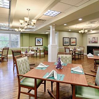 A well-lit dining area with neatly arranged tables and chairs, elegant chandeliers, and decorative elements.