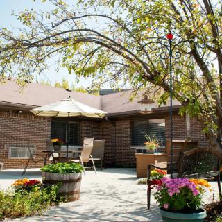 A serene patio with comfortable seating, surrounded by vibrant flowers and lush greenery.