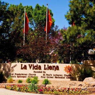 Entrance sign for La Vida Llena, surrounded by flags and trees.