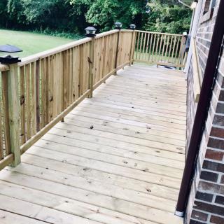 A wooden deck with a railing, adjacent to a brick wall, extends into a grassy yard.