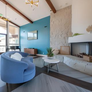 A modern living room featuring a blue sofa, stone fireplace, and wooden ceiling beams.