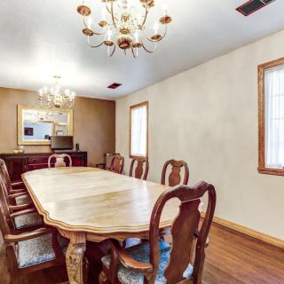A spacious dining room featuring a large wooden table and chairs, illuminated by elegant chandeliers.
