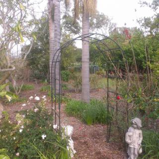 A tranquil garden scene featuring a metal archway, surrounded by lush greenery and adorned with a stone sculpture.