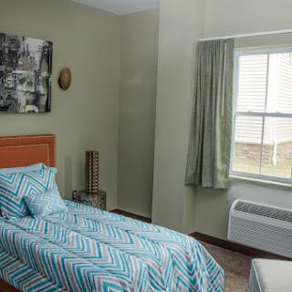 A cozy and modern bedroom featuring a single bed with a patterned quilt, a window with green curtains, and decorative wall art.