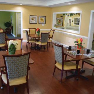 A cozy dining area with multiple tables and chairs, featuring warm yellow walls and wooden flooring.