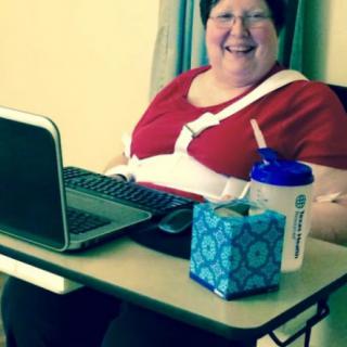 A person smiling while sitting at a desk with a laptop and a water bottle.
