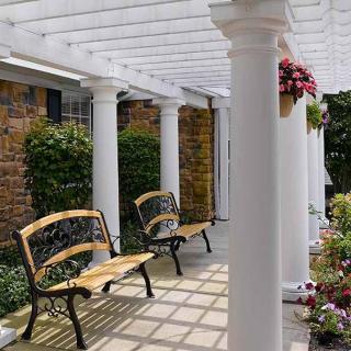 A charming outdoor patio with a pergola and benches surrounded by flowers.