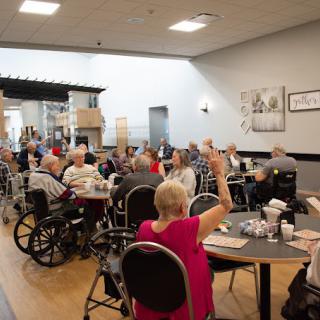 A community gathering of elderly individuals, some in wheelchairs, engaged in a group activity inside a nursing home.