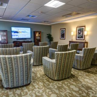 A comfortable waiting area with arranged chairs facing a television, complemented by framed art and soft lighting.
