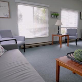 A cozy living room setting featuring comfortable chairs, a wooden table, and natural light filtering through the blinds.