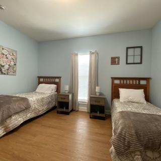 A cozy bedroom with two twin beds and a window between them, featuring light blue walls and wooden flooring.