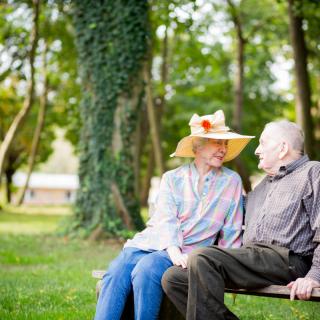 An elderly couple sitting on a bench in the park, enjoying each other's company amidst nature.