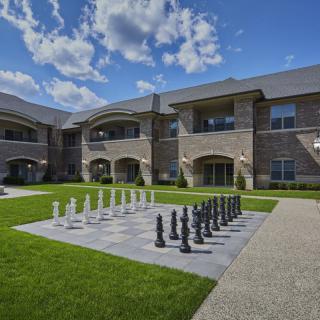 A courtyard with a large outdoor chess set in front of a brick building under a partly cloudy sky.