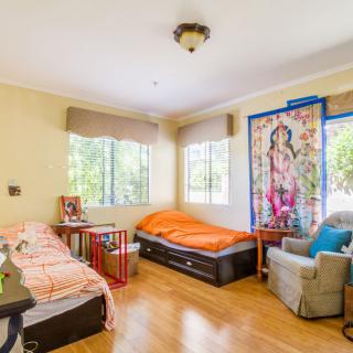 A bright bedroom with twin beds, an armchair, and a colorful tapestry.