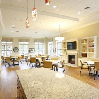 A spacious and modern dining area with multiple tables, chairs, a large fireplace, and ample natural light from the windows.